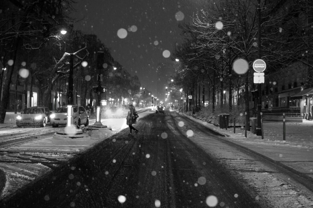 Snow falls on a quiet urban street at night, creating a serene winter atmosphere.
