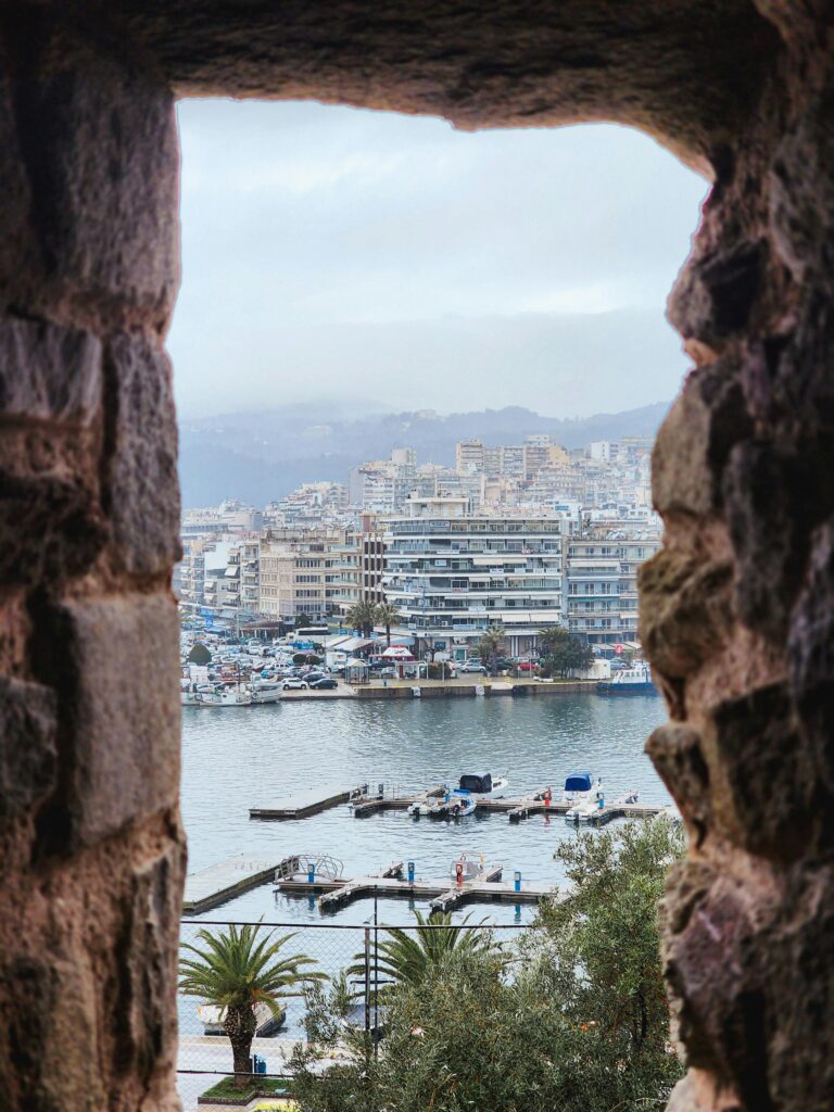 Captivating view of Kavala, Greece through historical stone arch. Boats and cityscape visible.