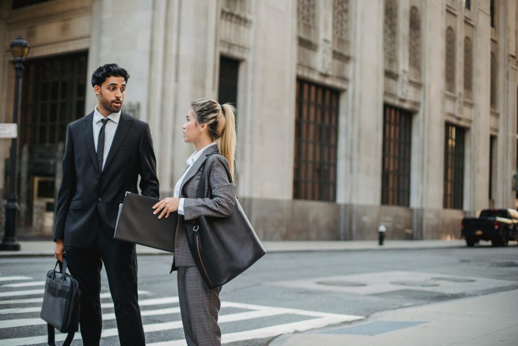 Two business professionals discuss on a city street, showcasing formal attire and urban setting.