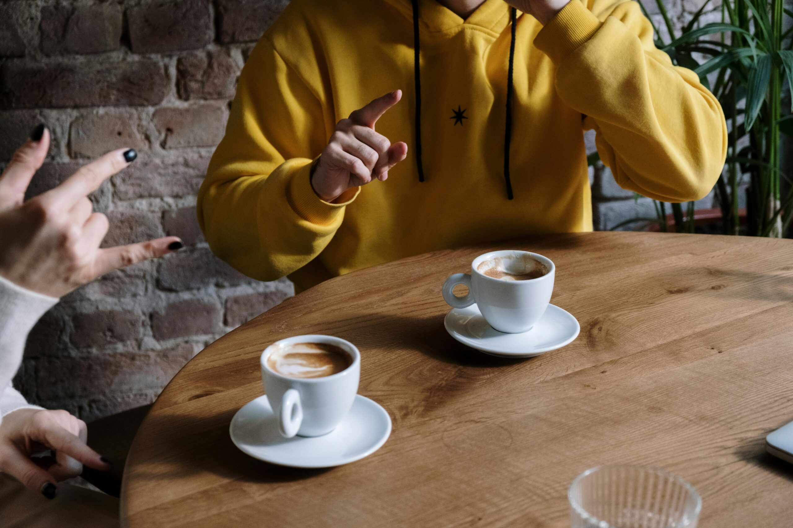 Two individuals use sign language while enjoying coffee at a cozy cafe.