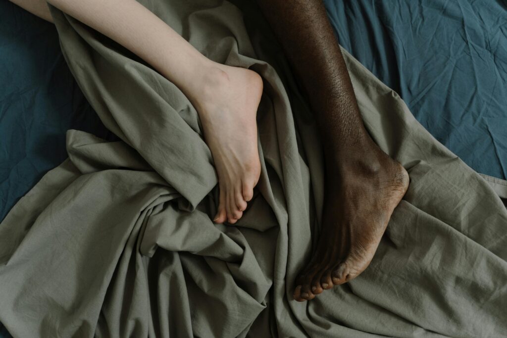 Close-up of an interracial couple's feet on crumpled sheets, symbolizing comfort and intimacy.