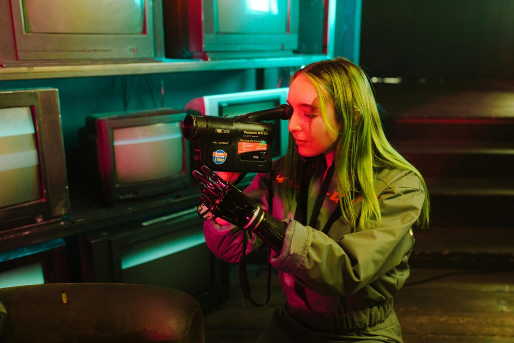 Woman using a prosthetic hand records video indoors, surrounded by vintage TVs.