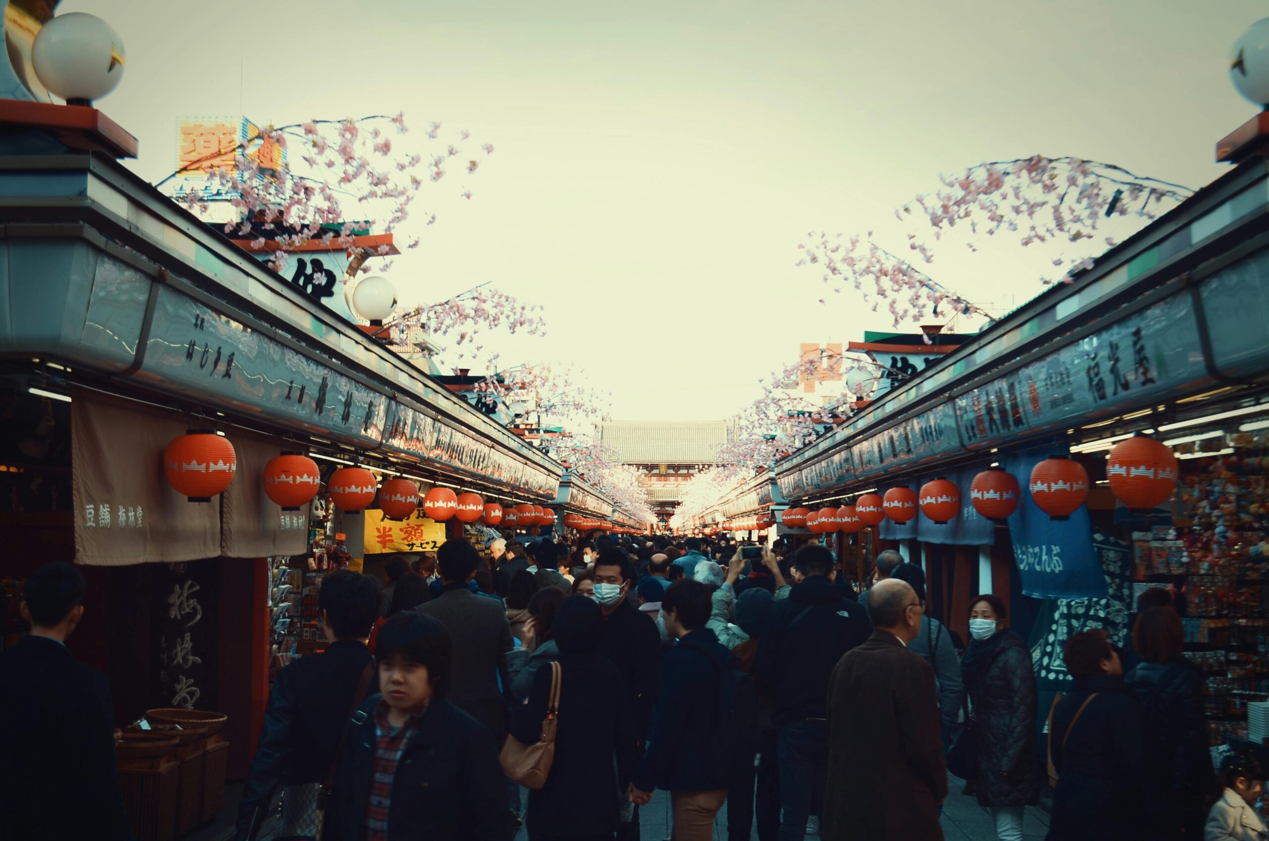 Vibrant Tokyo street market scene filled with people under cherry blossoms.