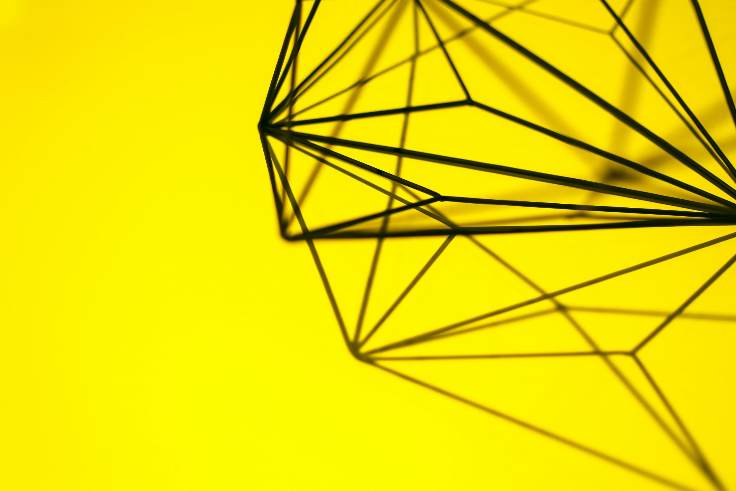 Creative geometric structure casting intricate shadows on a vibrant yellow background.