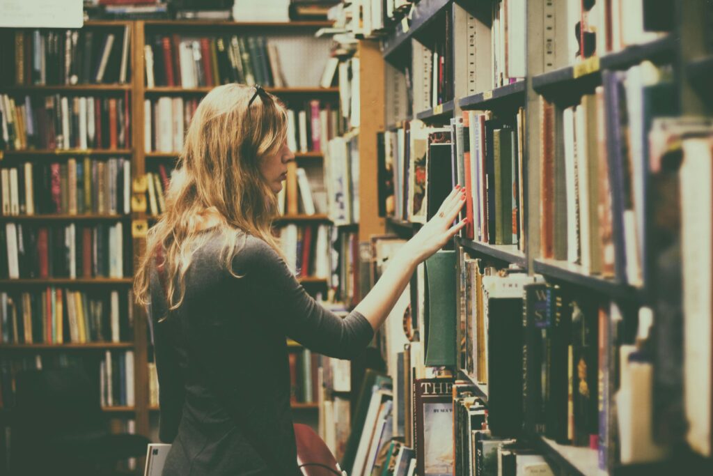 A woman explores bookshelves in a warm, inviting library filled with numerous books.