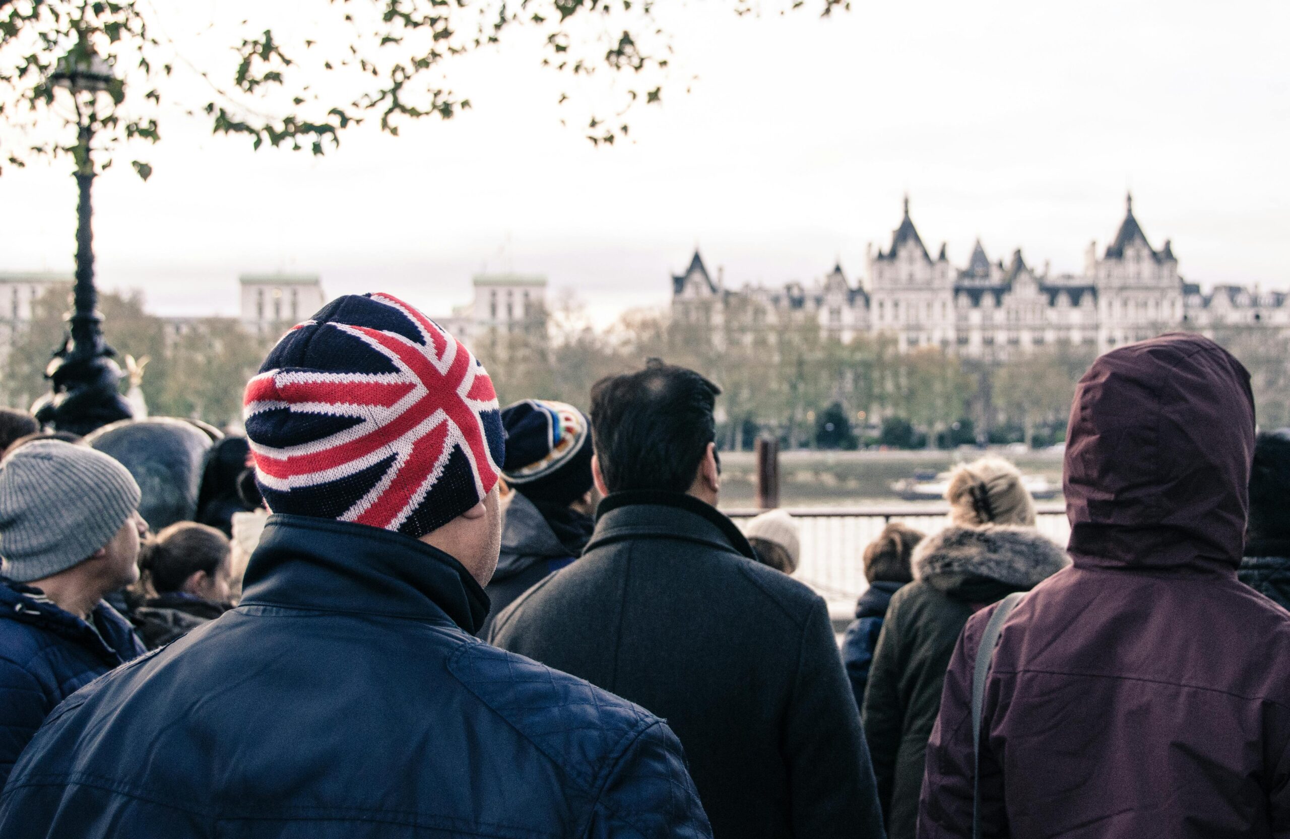 A crowd in London faces iconic architecture. Prominent British Union Jack hat in focus.
