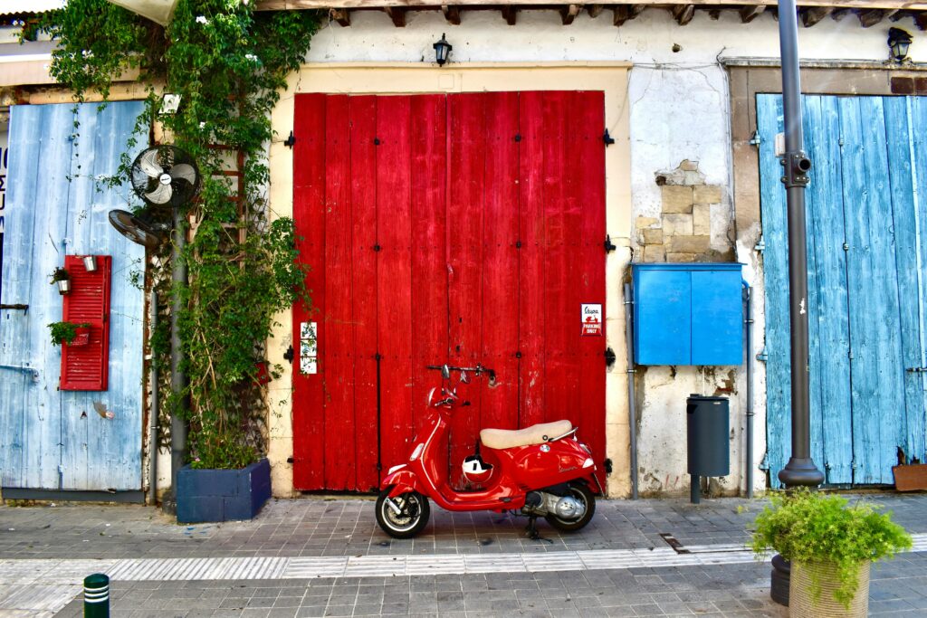 Colorful street scene in Larnaca, Cyprus, with a red scooter and wooden doors.