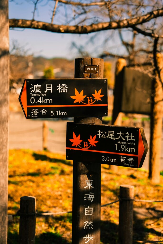 A wooden signpost in a park displaying directions and distances in Japanese text with autumn theme.