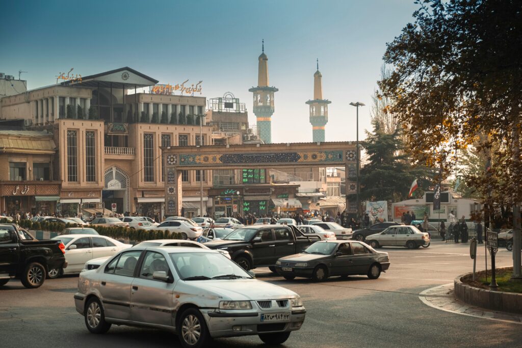 Bustling Tehran street scene with cars, mosque minarets, and traditional architecture.