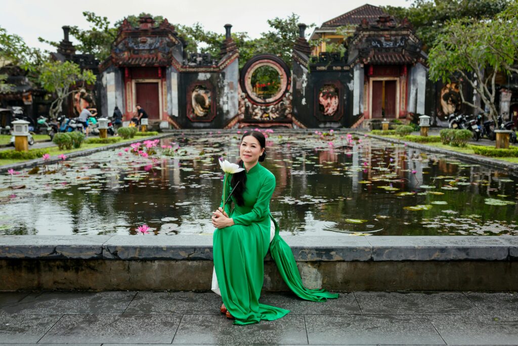 Woman in green ao dai sitting by a temple pond in Hội An, Vietnam.