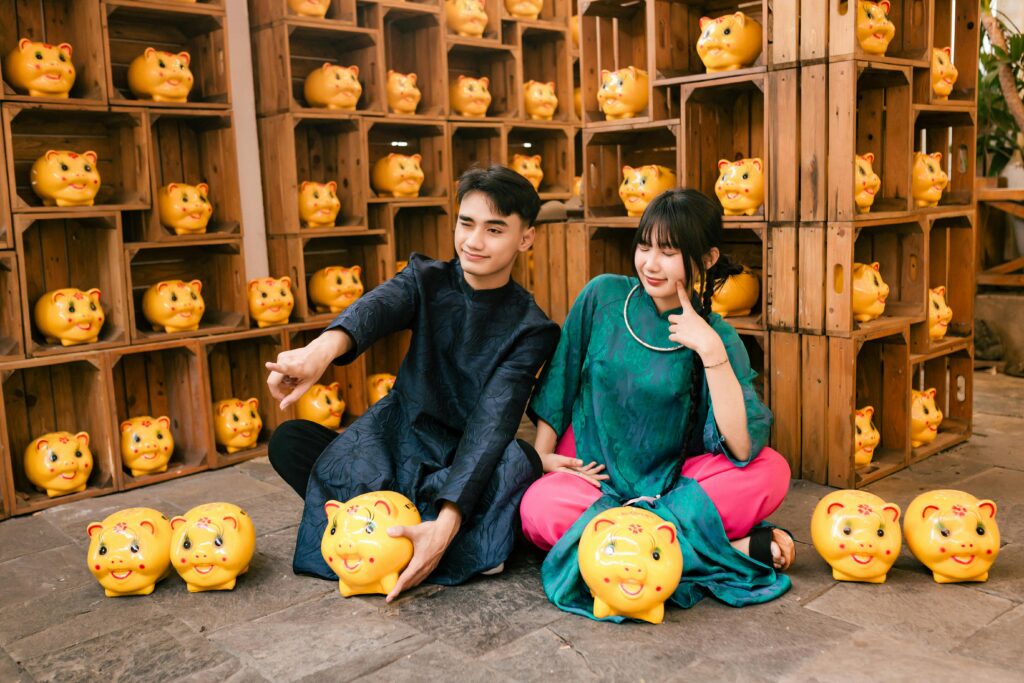 A young couple in traditional attire poses with piggy banks in Hội An, Vietnam.