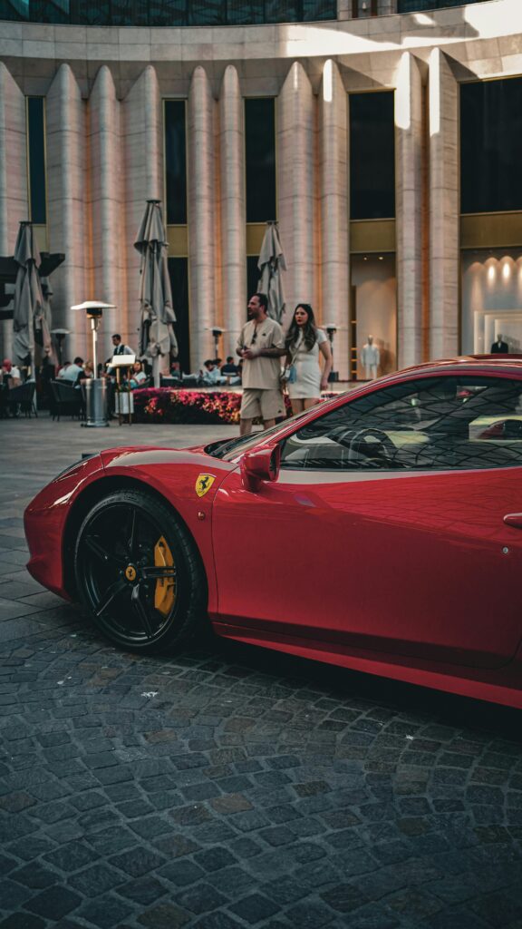 A sleek red luxury car parked in front of a modern architecture building in İzmir.