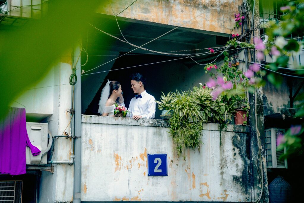 Couple in wedding attire sharing a moment on a rustic balcony surrounded by greenery.