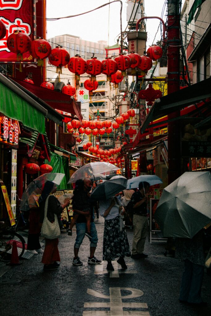 People with umbrellas walking under vibrant red lanterns in Yokohama Chinatown.