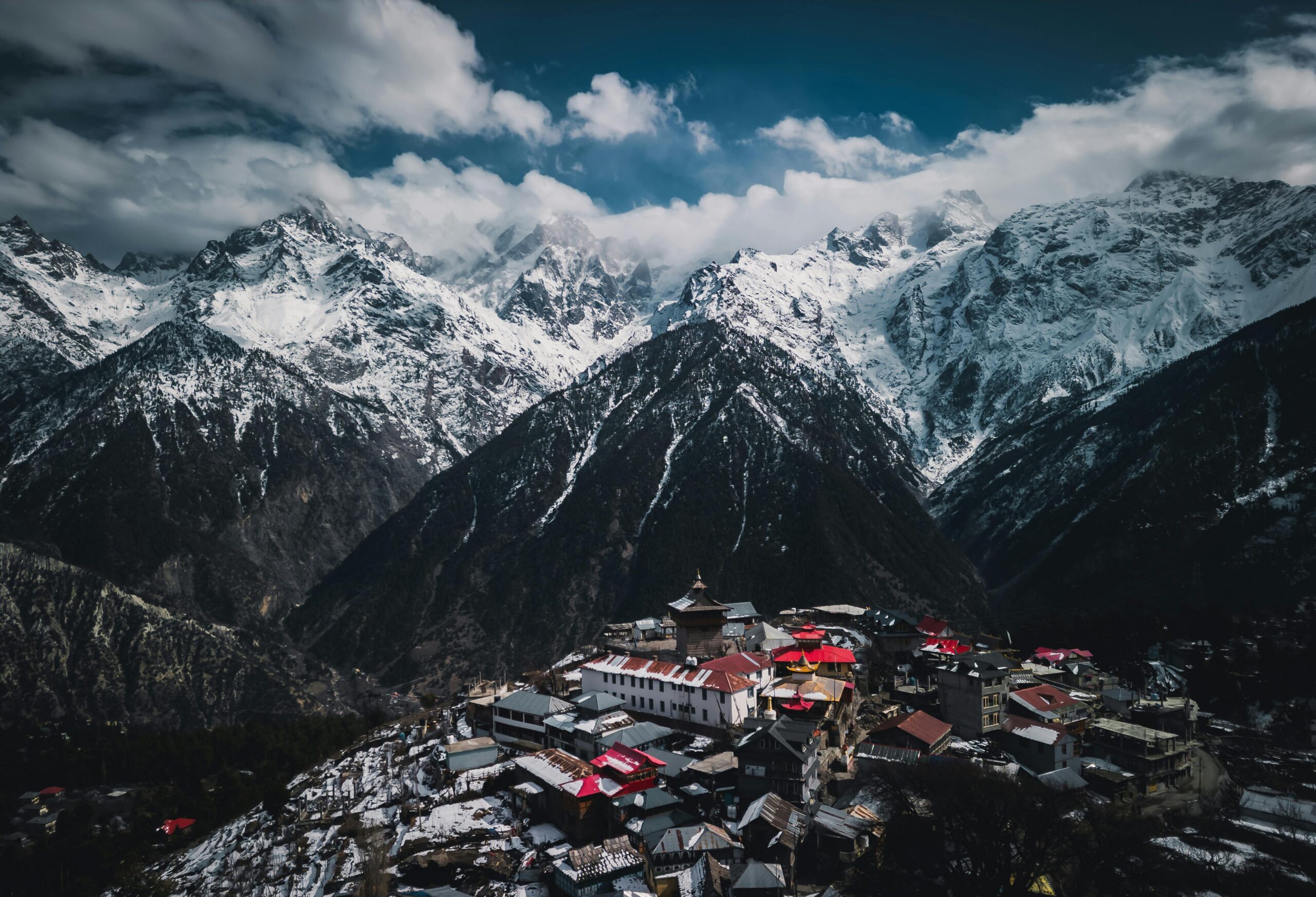 A breathtaking view of a snow-capped Himalayan village set against majestic mountains under a cloudy sky.