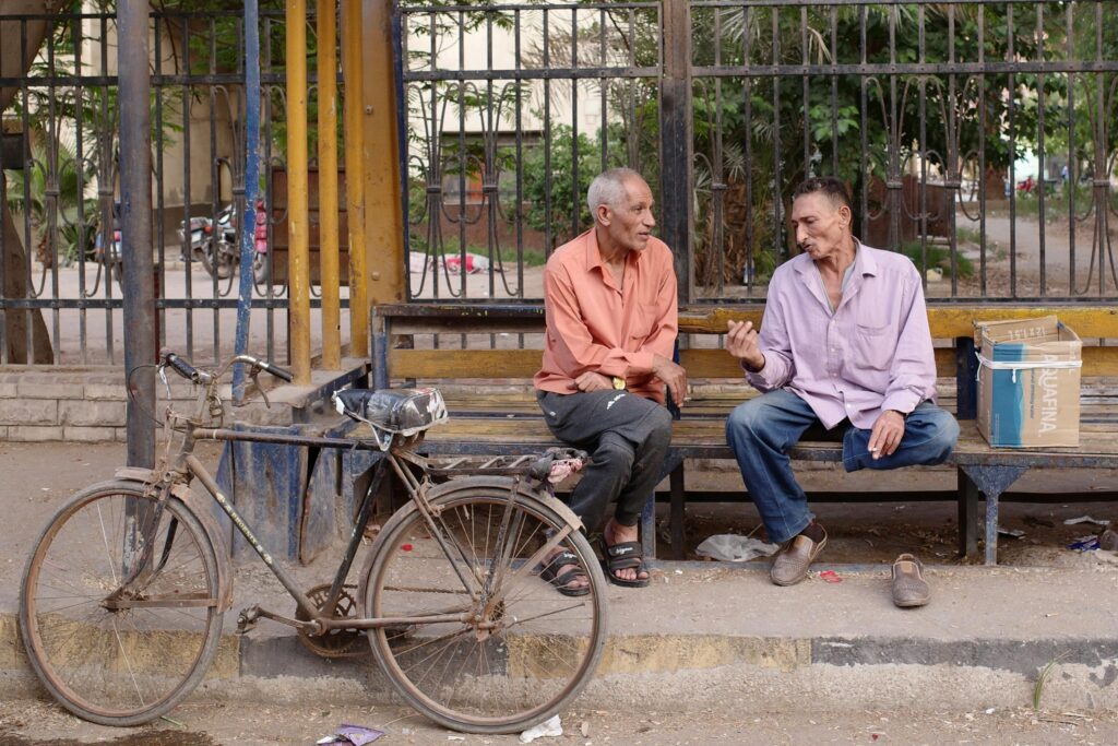 Two elderly men converse on a street bench in Cairo, with a bicycle nearby, capturing everyday life in Egypt.