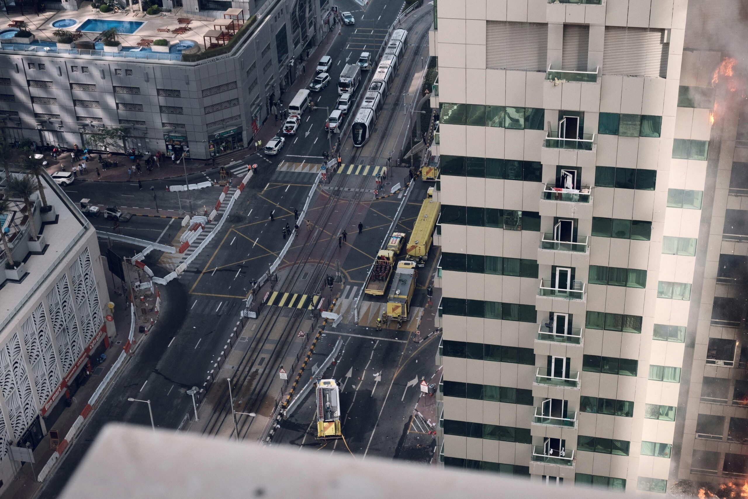 Aerial view of emergency response to a building fire in Dubai featuring fire trucks and construction barriers.