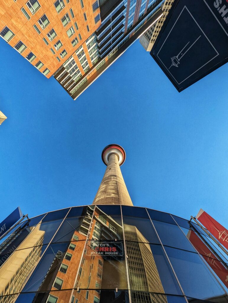 Upward view of the iconic Calgary Tower surrounded by tall buildings in vibrant daylight.