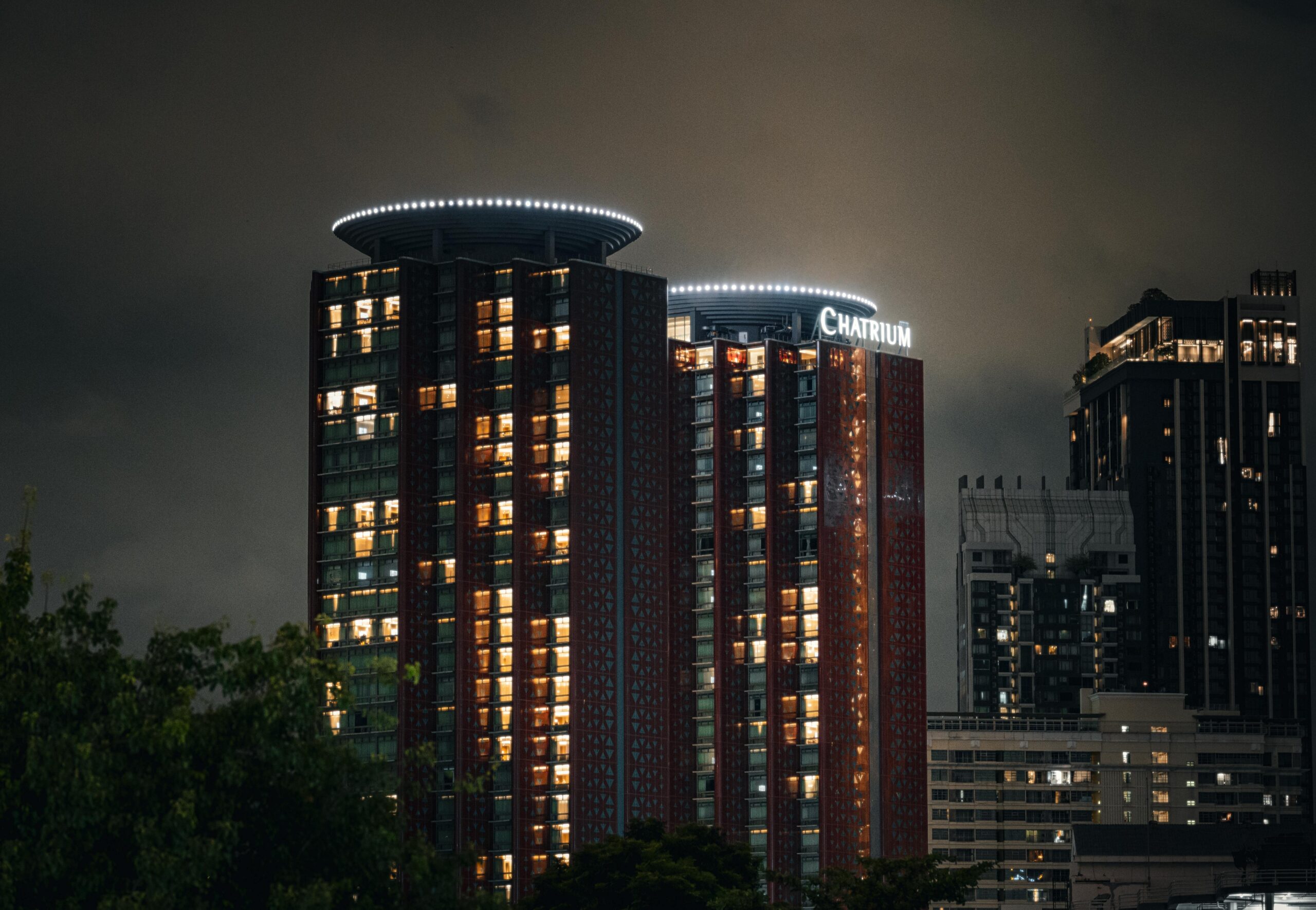 Illuminated Chatrium Hotel in Bangkok skyline at night, showcasing modern architecture.