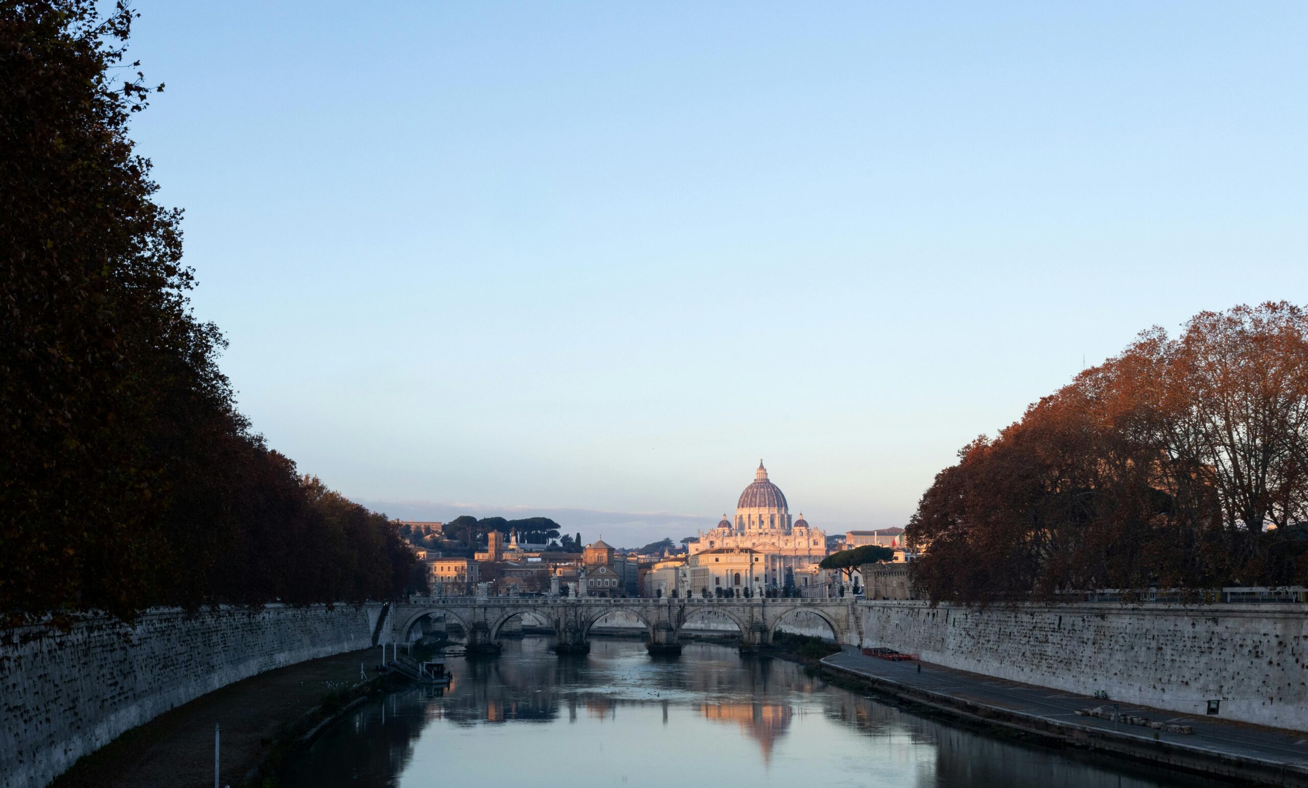 Iconic view of St. Peter's Basilica and the Tiber River in Rome at sunrise, capturing the serene city skyline.
