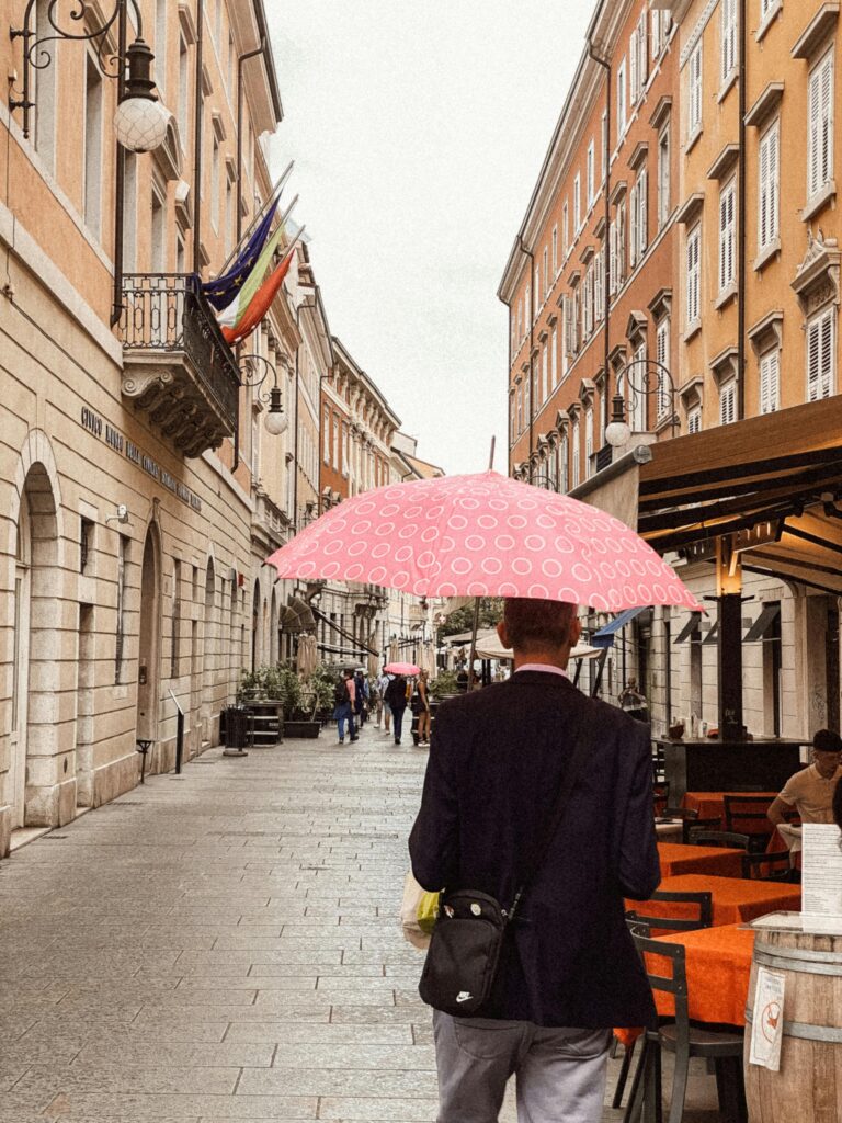 A man with a pink umbrella walks down a charming street in Italy, capturing the essence of Italian architecture.