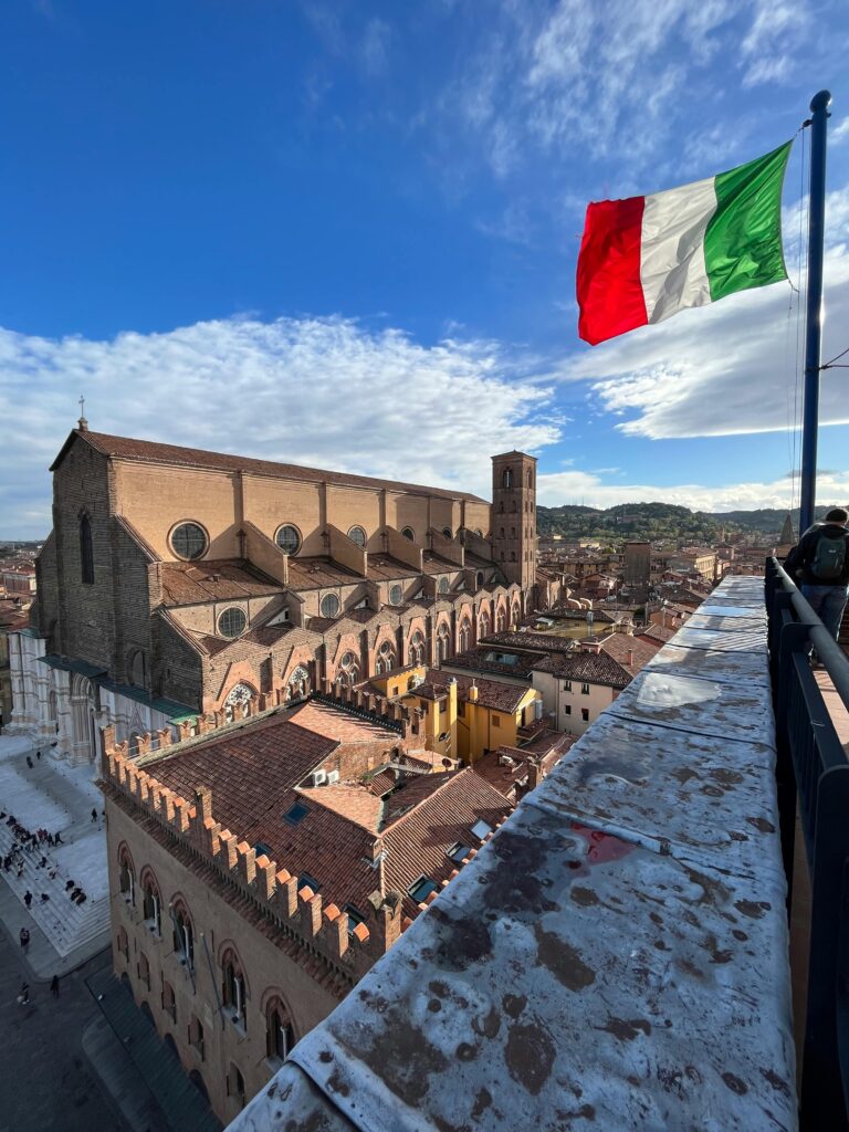 Scenic aerial view of Bologna, Italy with a waving Italian flag and historic architecture.