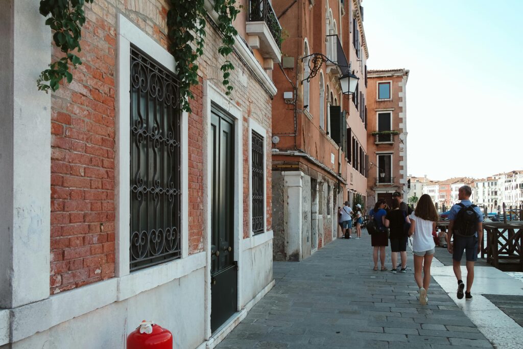 Tourists enjoying a summer walk along a picturesque canal in Venice, Italy with historic architecture.