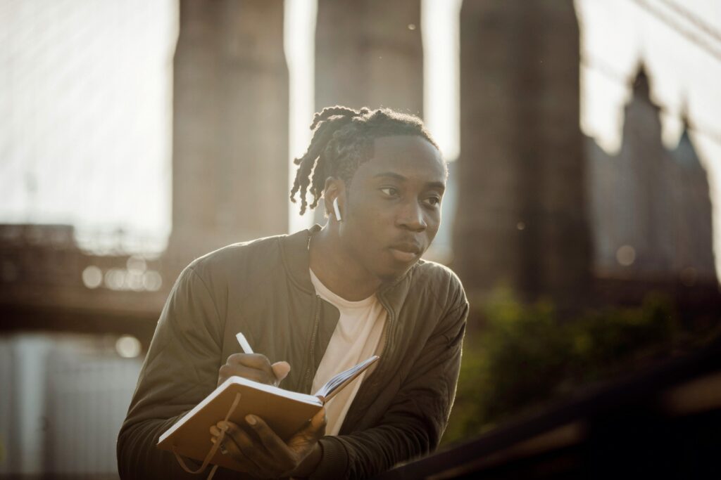 Pensive young man sketching near a famous urban bridge on a sunny day.