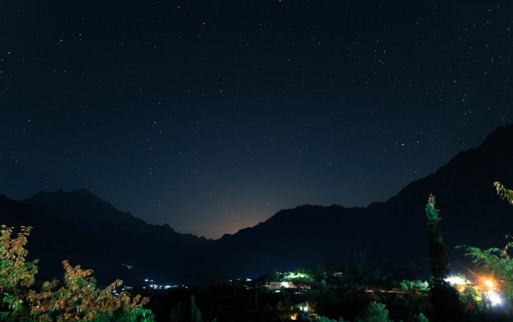 A serene starry night sky over a mountainous village, showcasing constellations.