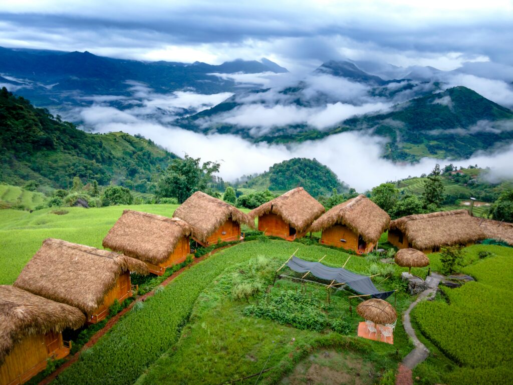 Beautiful rural landscape with traditional Vietnamese bungalows surrounded by misty mountains and green fields.