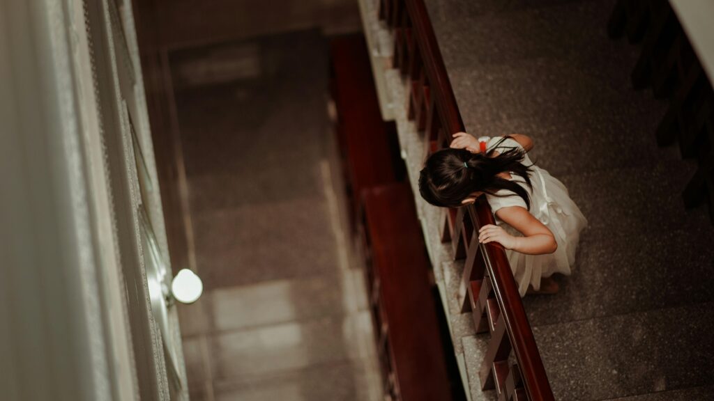 A child in a white dress going down stairs indoors, seen from above.