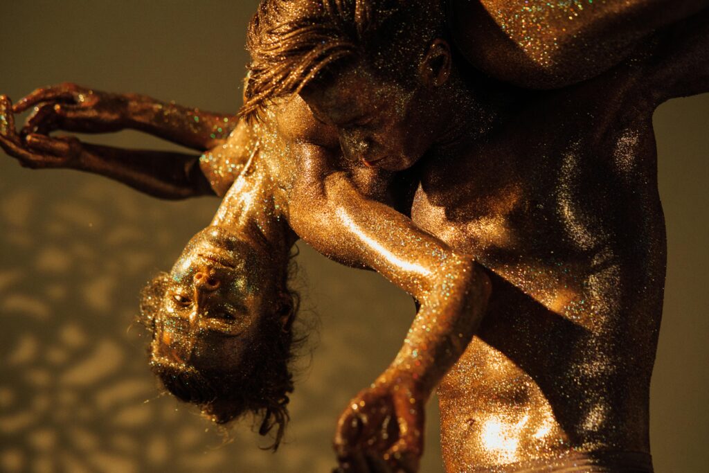 Dramatic dance performance with glitter-covered dancers in an artistic pose.