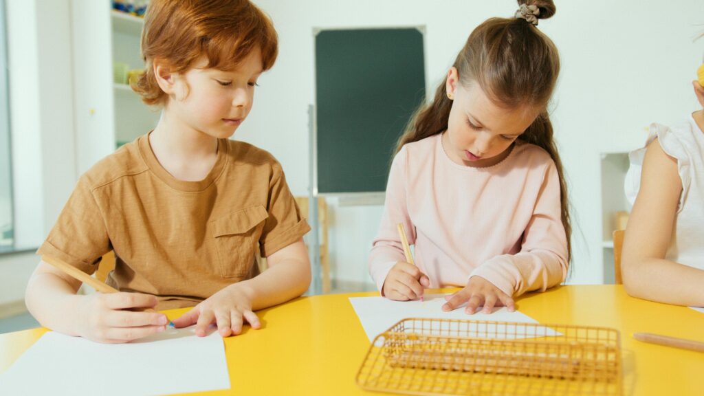Two young children engaged in writing activities at a classroom desk, fostering learning and creativity.