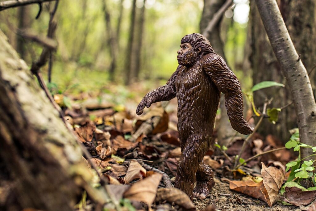 A detailed Bigfoot toy model walking through a forest with fallen leaves, creating a natural wilderness scene.