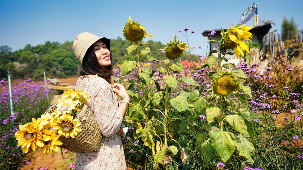 A cheerful woman with a sunflower-filled basket smiles in a vibrant Chiang Mai garden.