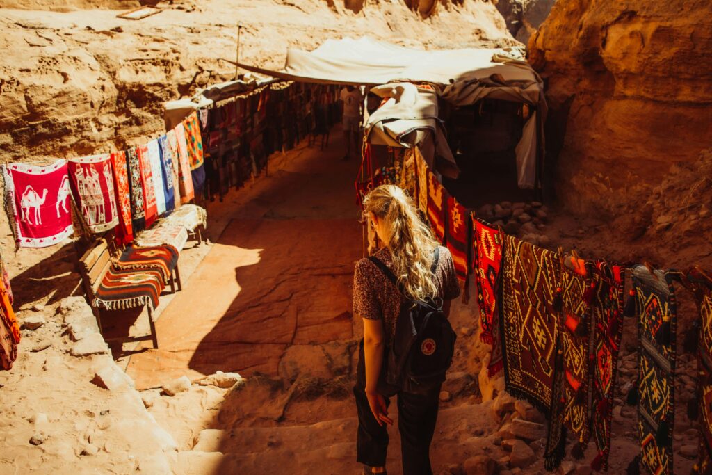Woman browsing colorful textiles in a market passage in Wadi Musa, Jordan.
