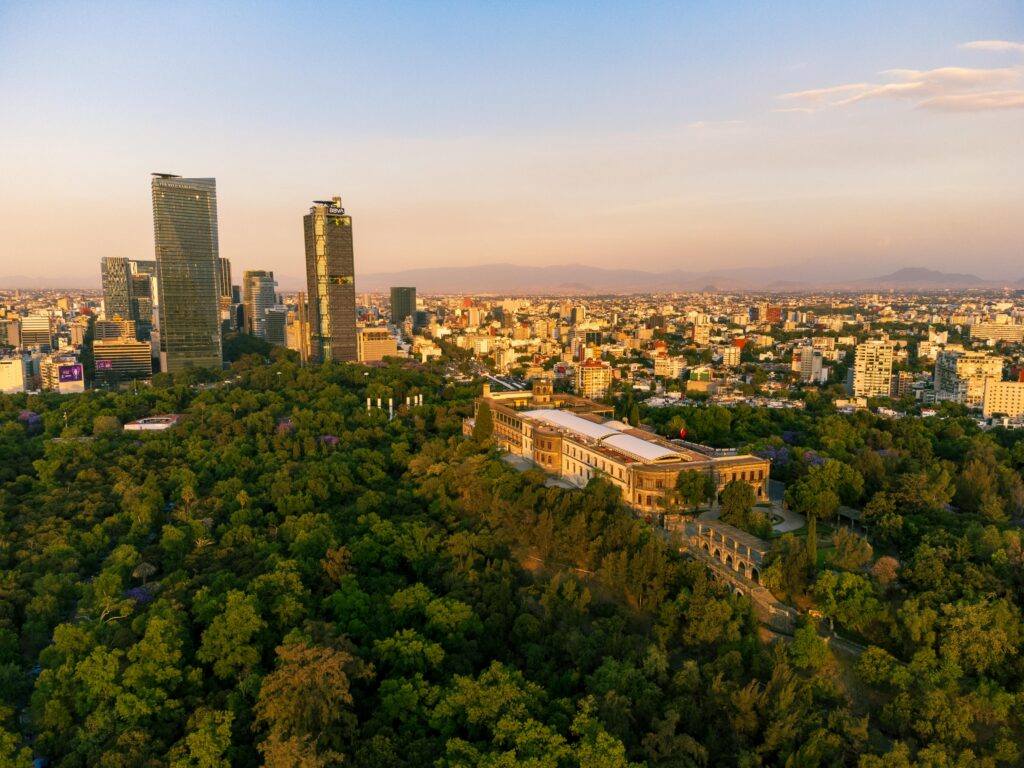 Breathtaking aerial view of Chapultepec Castle amidst lush greenery against the Mexico City skyline at sunset.