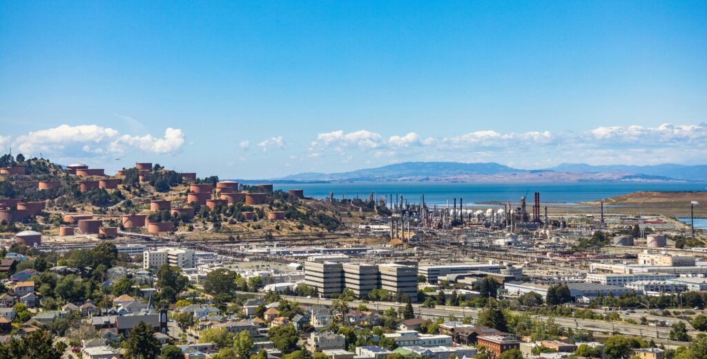 Aerial view of an urban area with an oil refinery by the sea and mountains.