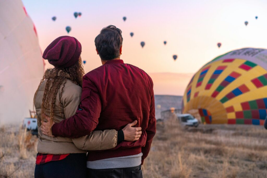 A couple embraces while watching hot air balloons during a colorful sunrise in Cappadocia, Turkey.