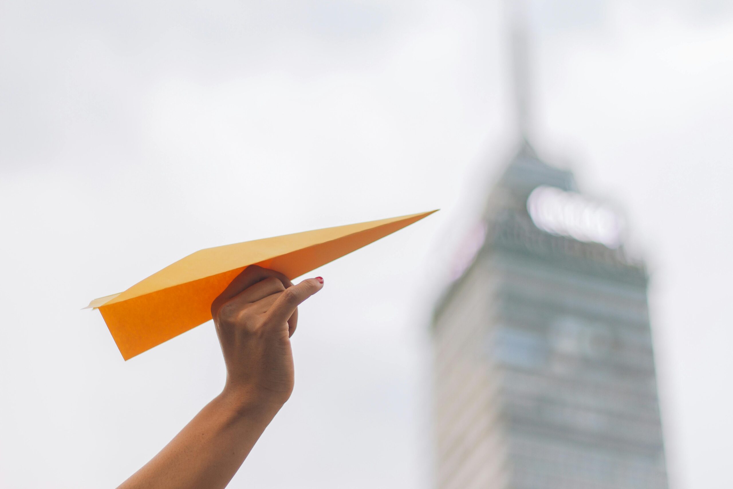 Close-up of a hand holding a paper airplane with Torre Latinoamericana in the background, Mexico City.