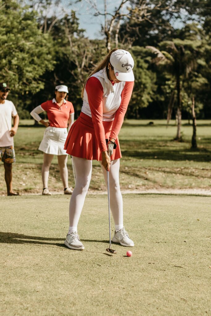 Woman wearing sportswear practicing putting on a golf course under the sun.
