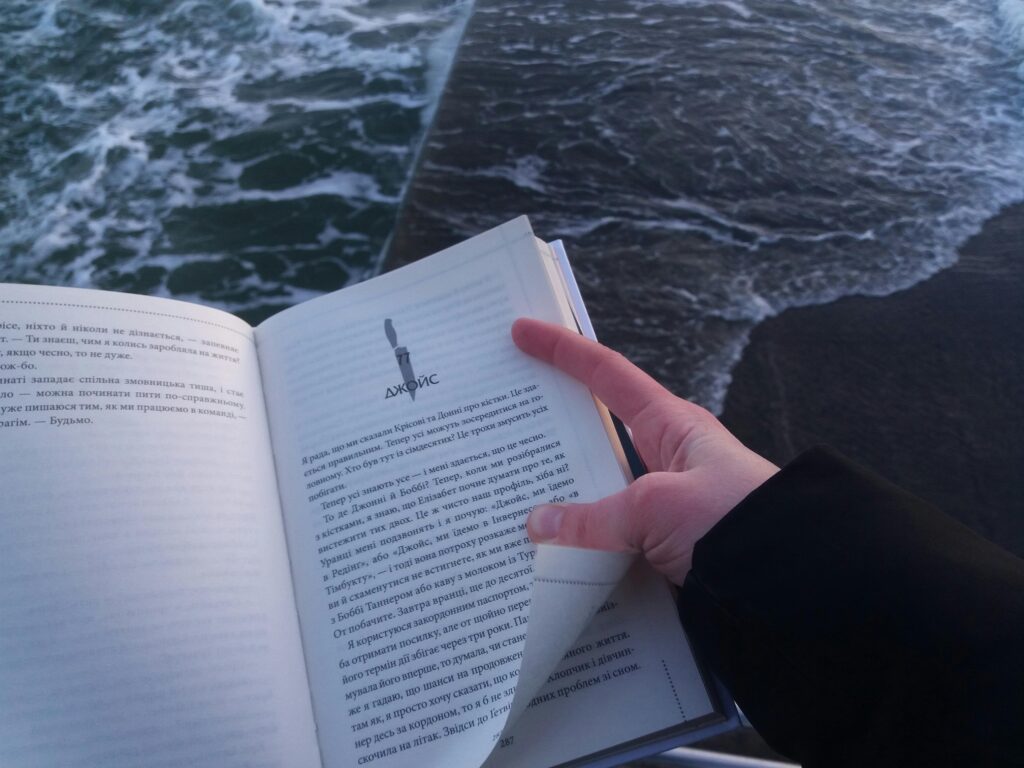 An open book in a person's hand near the ocean, signifying calm and knowledge.