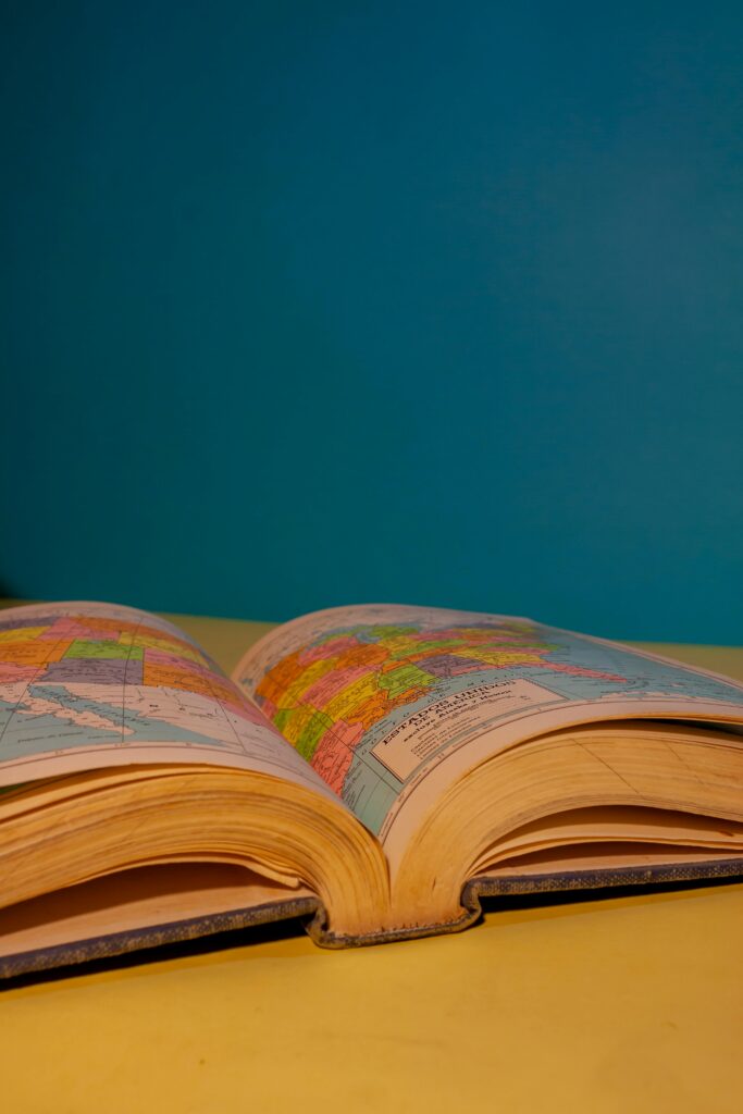 Open atlas displaying vibrant maps on a yellow table against a blue background.