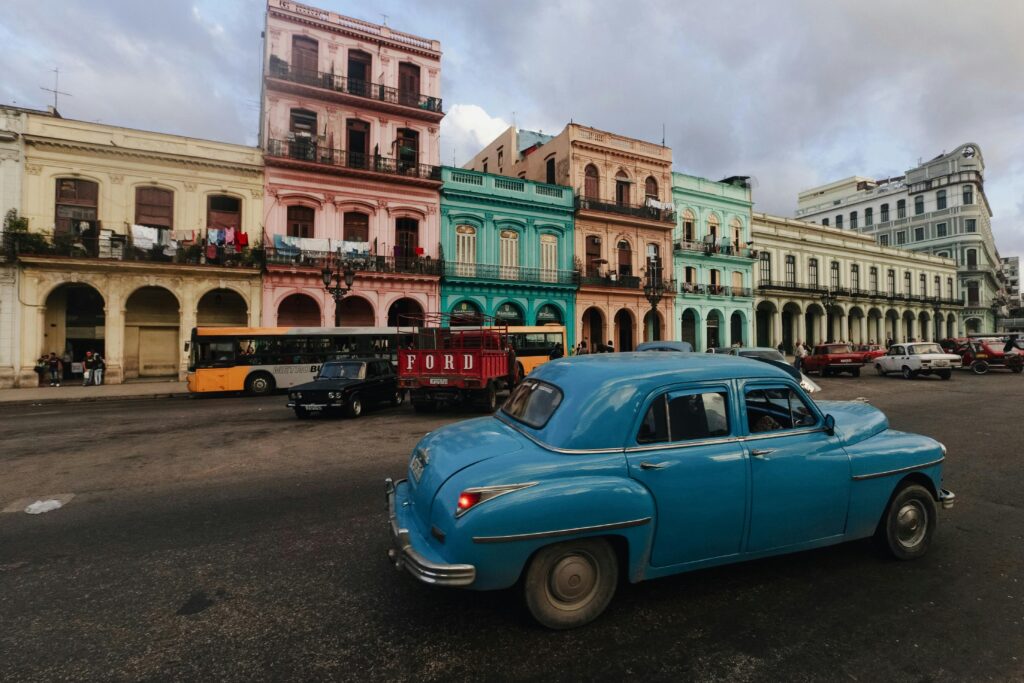 Classic cars cruise past vibrant colonial buildings in lively Havana street scene.
