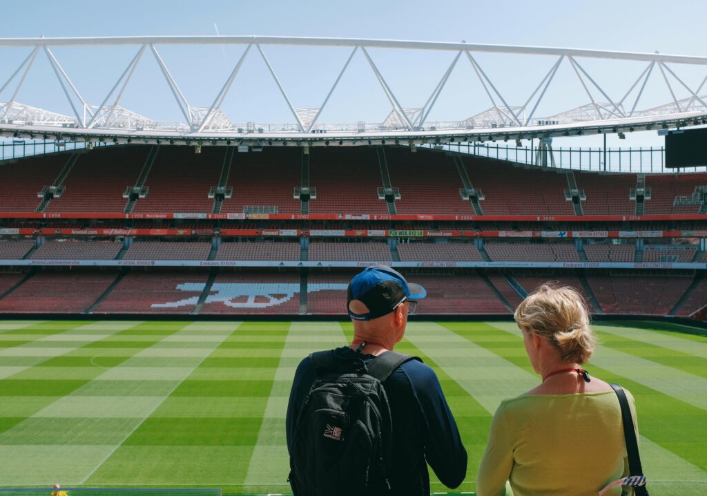 Two tourists exploring the iconic Emirates Stadium with a view of the empty football pitch.
