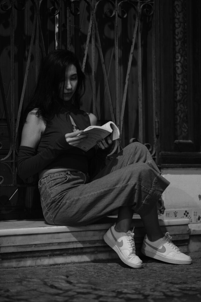 A woman sits outdoors at night, engrossed in a book, creating a serene, monochrome scene.