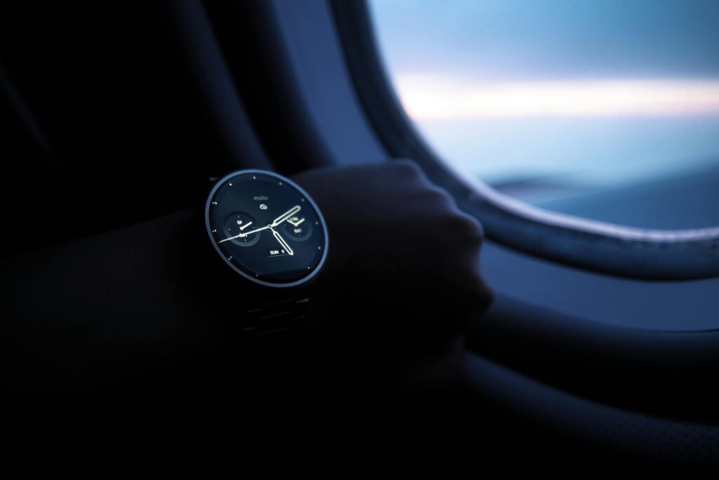 A smartwatch on a wrist shown against an airplane window view during flight.