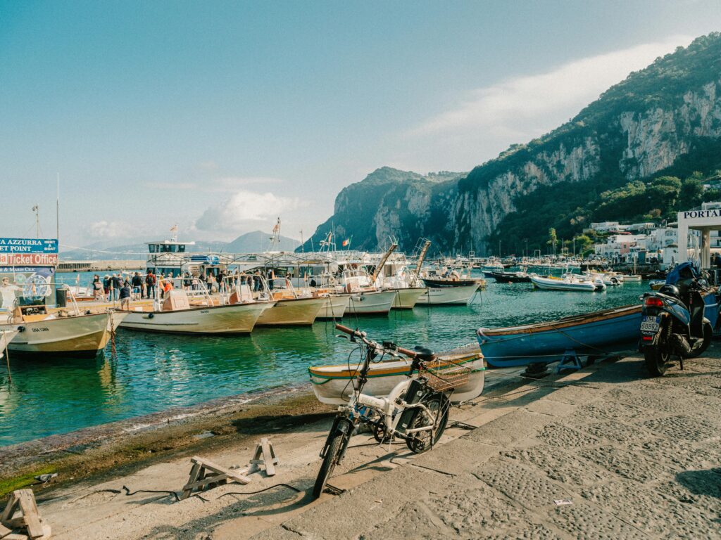 Beautiful summer day at Capri's marina with boats moored along the shore and cliffs in the background.