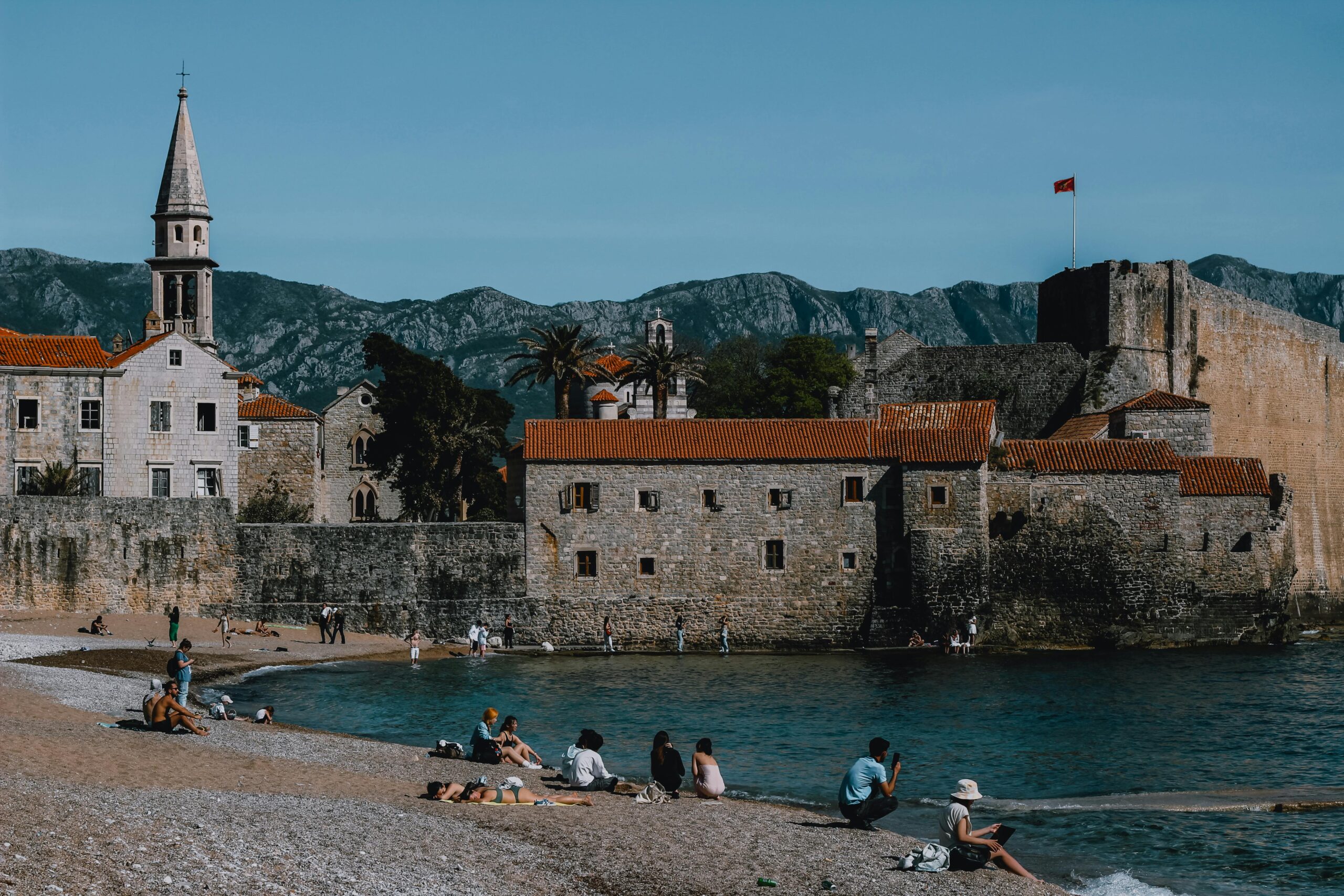Sunny day at Budva Beach featuring the historic medieval town walls and mountains.