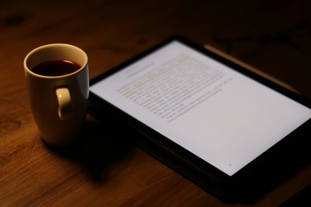 Tablet with text beside a mug of coffee on a wooden table.
